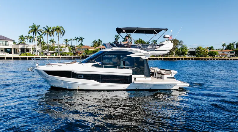 Slide: The Image of 2022 Galeon 400 Fly yacht cruising on a sunny day, surrounded by palm trees and waterfront homes. - 3