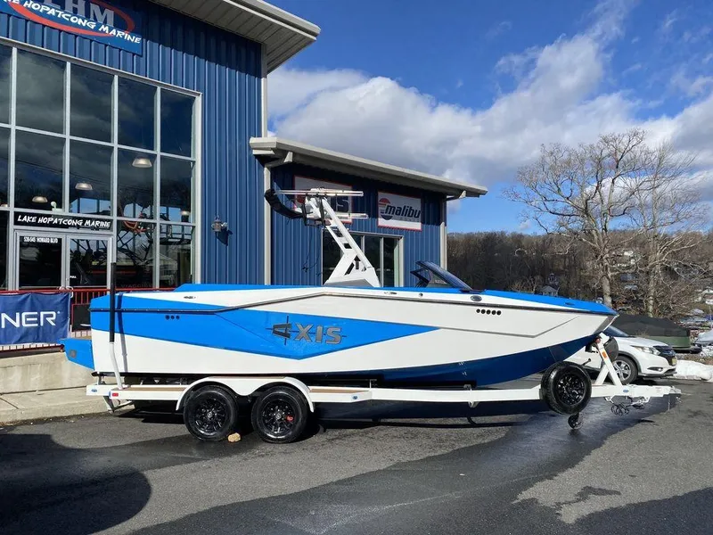 Slide: The Image of 2025 Axis T235 boat on trailer outside marine dealership, blue and white design. - 2