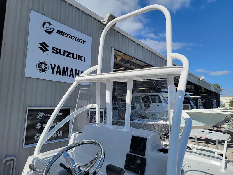 Slide: The Image of 2025 Shallow Sport 24 Modified V boat at dealership with Mercury, Suzuki, Yamaha signage. - 23