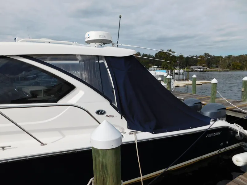 Slide: The Image of 2018 Pursuit OS 325 Offshore boat docked with blue cover, calm waters in background. - 3