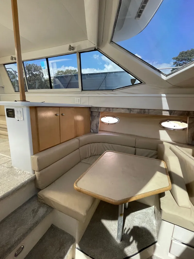 Slide: The Image of 1997 Carver 405 yacht interior with beige seating and table, large windows, and wooden cabinets. - 27
