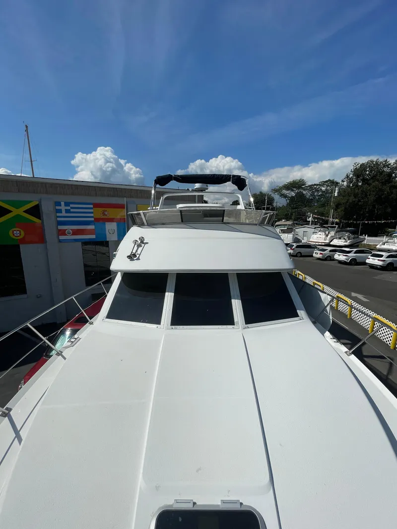 Slide: The Image of 1997 Carver 405 yacht docked, with flags and parked cars in the background. - 32