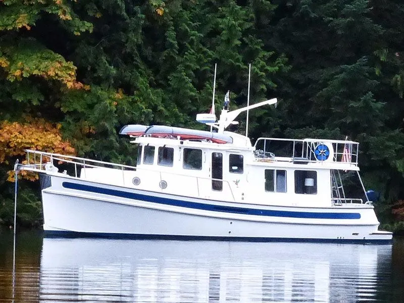 Slide: The Image of 2007 Nordic Tug 37 boat on calm water, surrounded by lush green trees. - 0