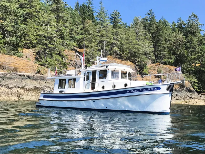 Slide: The Image of 2007 Nordic Tug 37 boat on water, surrounded by lush trees and rocky shoreline. - 1
