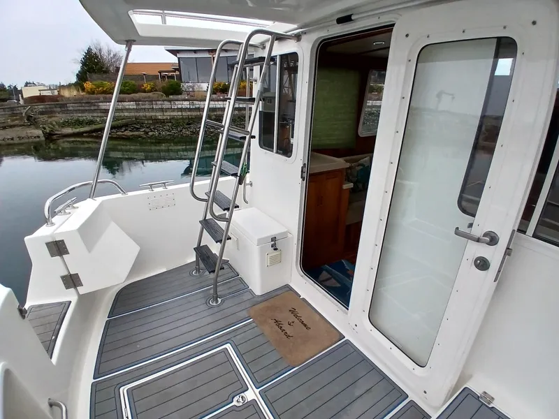 Slide: The Image of 2007 Nordic Tug 37 boat deck with ladder and glass door, docked by the shore. - 12