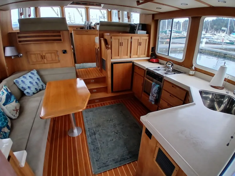 Slide: The Image of Interior of a 2007 Nordic Tug 37, featuring a cozy dining and kitchen area with wood finishes. - 13