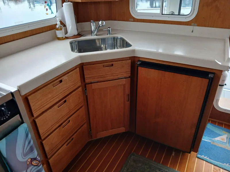 Slide: The Image of 2007 Nordic Tug 37 kitchen with wooden cabinets, sink, and compact refrigerator. - 16