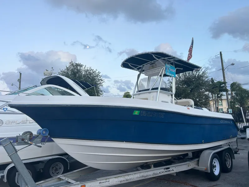 The Image of 2009 Cobia 216 Center Console boat on trailer, blue hull, parked outdoors. - 1