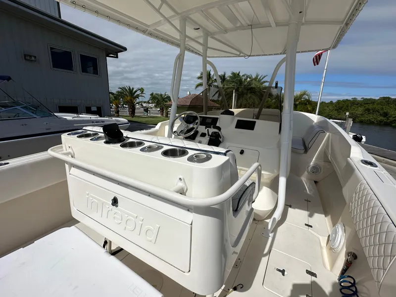 Slide: The Image of 2005 Intrepid 323 boat interior with helm, seating, and rod holders, docked near waterfront homes. - 25