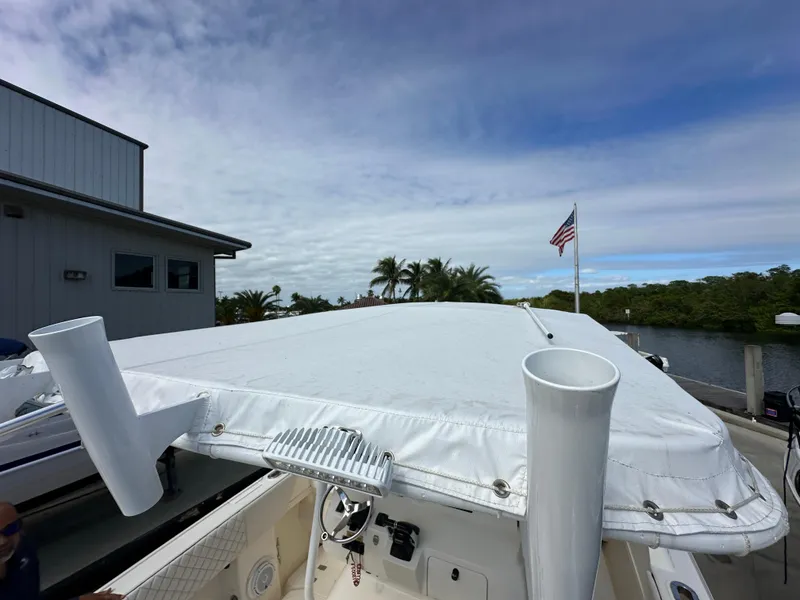Slide: The Image of 2005 Intrepid 323 boat with white cover docked near a building and American flag. - 26