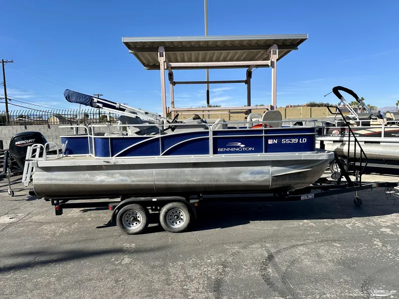Slide: The Image of 2021 Bennington 20SV pontoon boat on trailer, parked outdoors under clear blue sky. - 0
