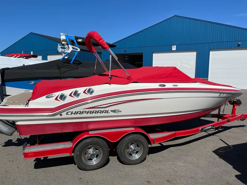 Slide: The Image of 2012 Chaparral 216 SSi boat with red cover on a trailer, parked near blue building. - 16