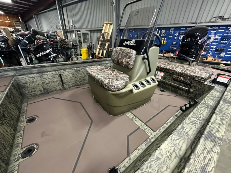Slide: The Image of 2025 Tracker Grizzly 1860 CC boat interior with camo seating and Mercury engines in a workshop. - 10