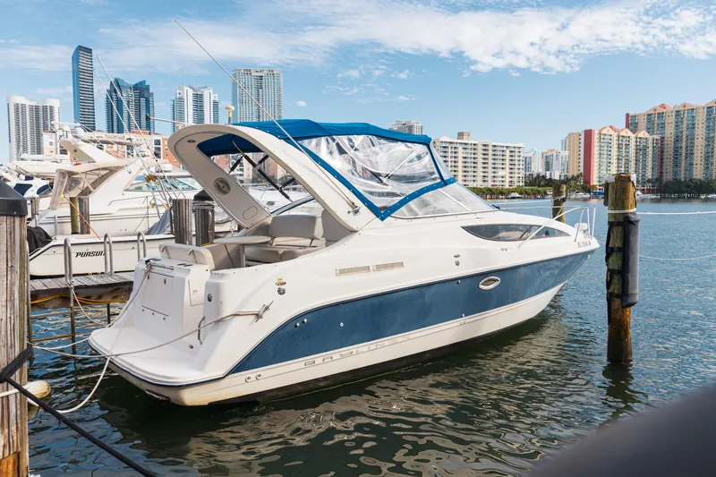 Slide: The Image of 2005 Bayliner 285 boat docked in a marina with city skyline background. - 0