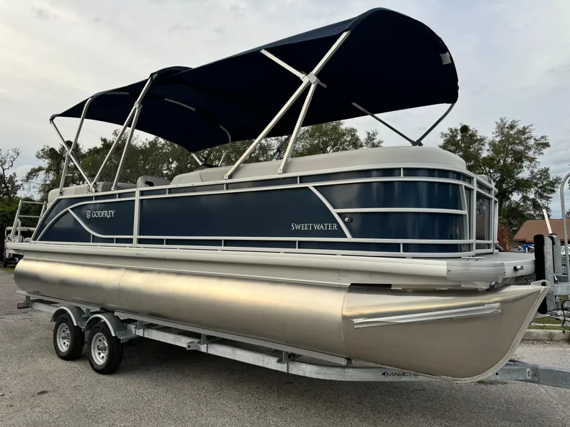 The Image of 2025 Sweetwater 2286 SB pontoon boat with blue canopy on a trailer. - 0