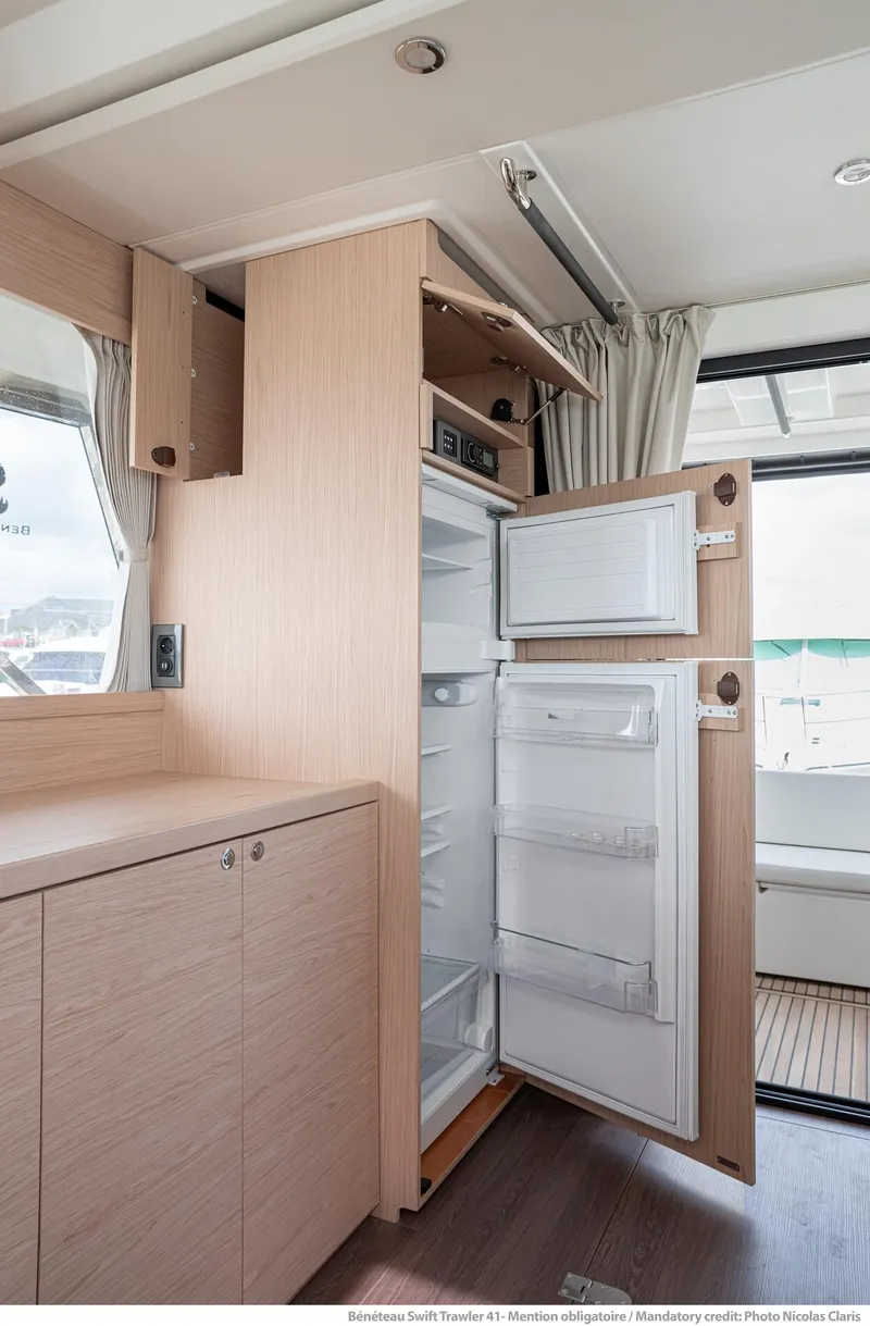 Slide: The Image of 2024 Beneteau Swift Trawler 41 interior with open fridge and wooden cabinetry. - 19