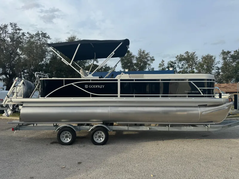 The Image of 2025 Sweetwater 2286 CSE pontoon boat on trailer, black canopy, parked outdoors. - 1