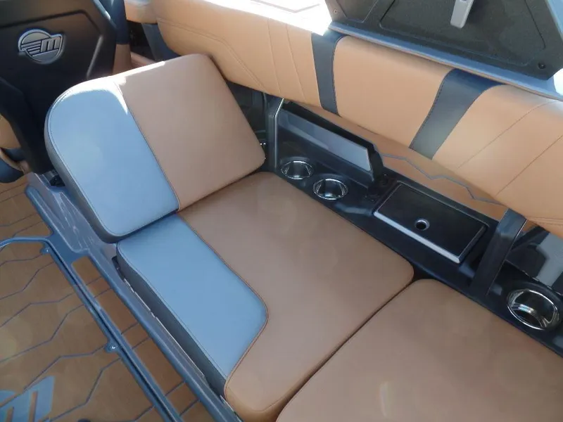 Slide: The Image of 2025 Malibu 23 MXZ boat interior with tan and gray seating, cup holders, and storage compartment. - 8