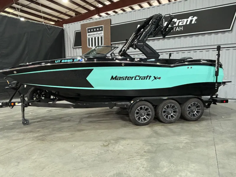 Slide: The Image of 2024 MasterCraft XStar S boat in showroom, black and teal design, on a trailer. - 2