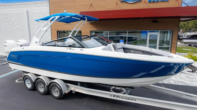 Slide: The Image of 2025 Cobalt R8 Outboard boat on trailer, blue and white design, parked outside dealership. - 2