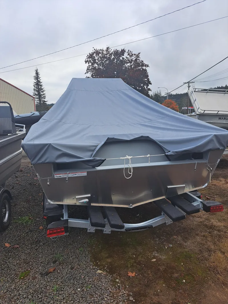 Slide: The Image of 2025 Klamath Baja Bayrunner boat covered, parked on a trailer in a yard. - 2