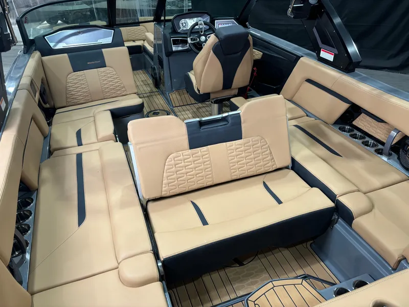Slide: The Image of 2023 MasterCraft X24 boat interior with tan and black seating, modern dashboard, and wood flooring. - 10