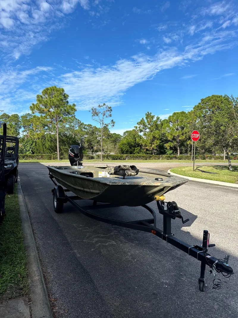 Slide: The Image of 2025 Tracker Grizzly 1654 T Sportsman boat on trailer, parked on a sunny road. - 2