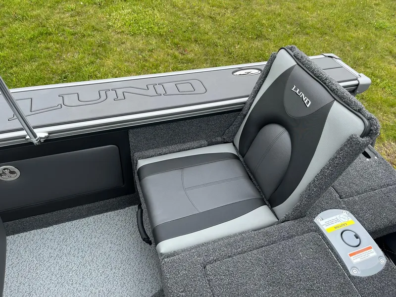 Slide: The Image of 2025 Lund 1975 Pro-V boat seat with gray upholstery and logo, on grassy background. - 21