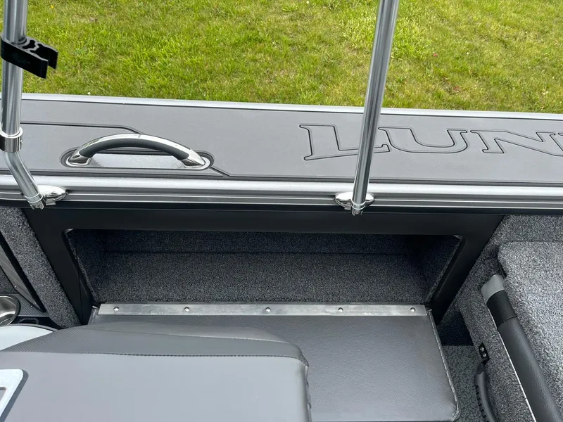 Slide: The Image of 2025 Lund 1975 Pro-V boat interior with storage compartment and handle, on grassy background. - 23