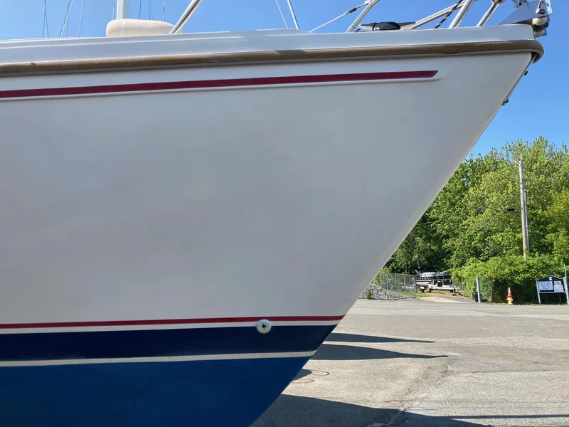 Slide: The Image of 1989 Catalina 30 sailboat bow with red and blue stripes, parked on a sunny day. - 23