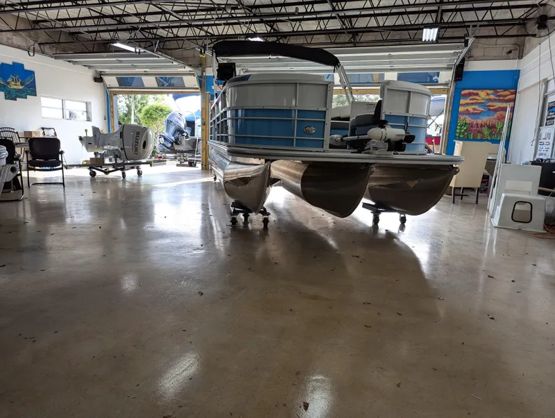 Slide: The Image of 2025 Trifecta CS 22RFC pontoon boat in showroom, polished floor, open garage doors. - 5