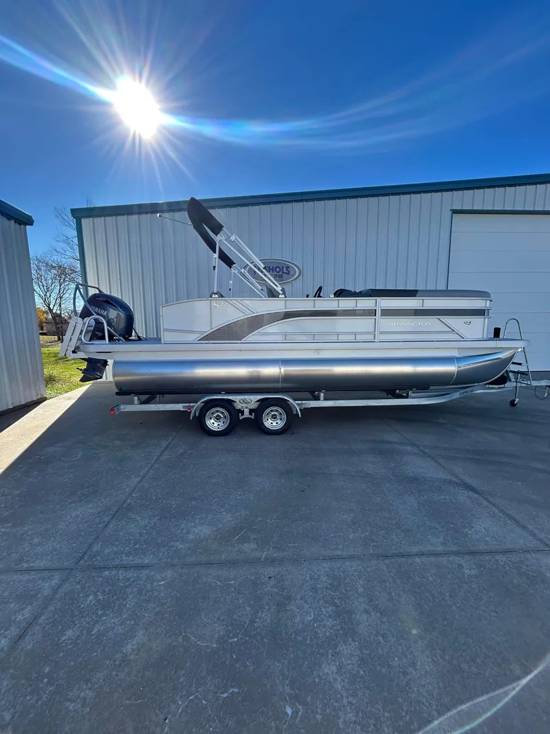 Slide: The Image of 2025 Bennington S 22 pontoon boat on trailer, parked outdoors under bright sun. - 1