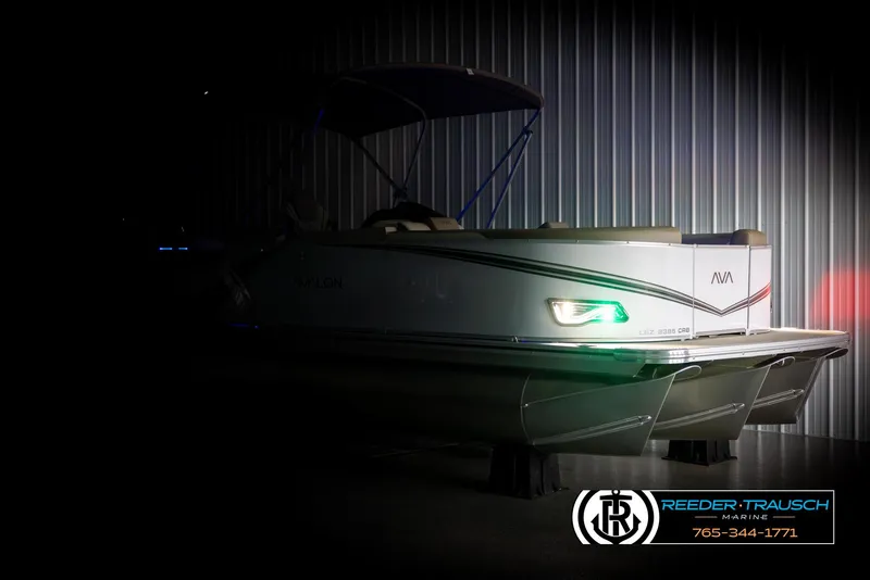 Slide: The Image of 2025 Avalon LSZ CRB pontoon boat in dimly lit showroom, side view. - 4