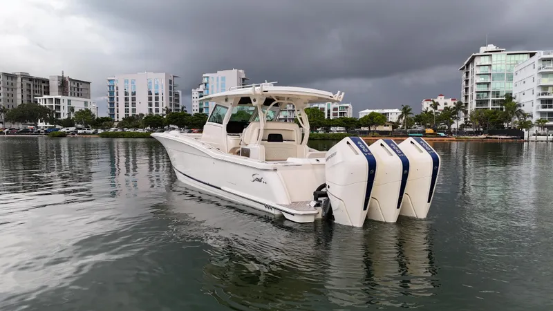 Slide: The Image of 2025 Scout 377 LXF boat with triple engines on calm water, urban backdrop. - 10