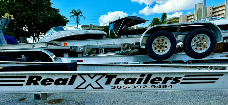 Slide: The Image of 2016 REAL X Model R32X trailer with boat, palm trees, and buildings in the background. - 0