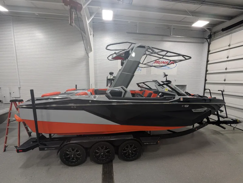 Slide: The Image of 2020 Nautique G23 Paragon boat in garage, black and orange design, on trailer. - 0