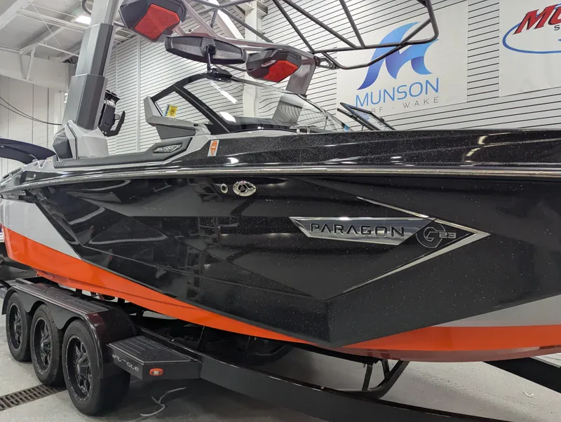 Slide: The Image of 2020 Nautique G23 Paragon boat in showroom, black and orange design, on a trailer. - 2