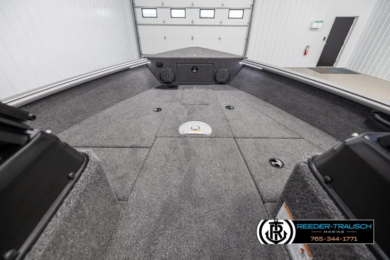 Slide: The Image of 2025 Lund 1875 Impact XS boat interior with carpeted deck in a garage setting. - 14