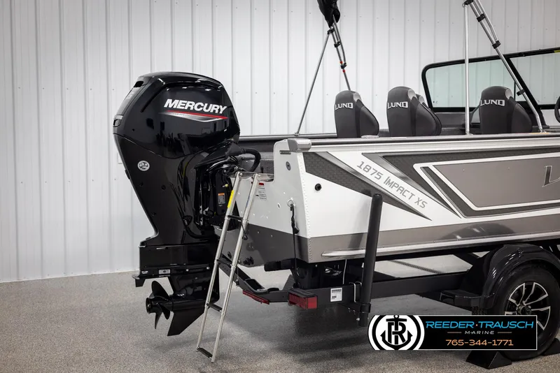 Slide: The Image of 2025 Lund 1875 Impact XS boat with Mercury engine, ladder, and sleek design in showroom. - 39