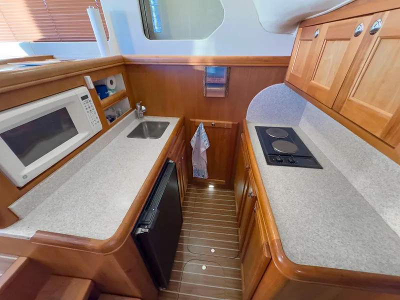 Slide: The Image of 2005 Mainship 34 Trawler kitchen with microwave, sink, stove, and wooden cabinets. - 13