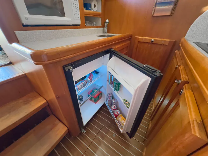 Slide: The Image of 2005 Mainship 34 Trawler kitchen with open fridge, microwave, and wooden cabinetry. - 18