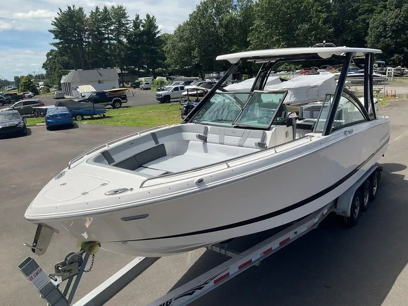 The Image of 2025 Chaparral 310 OSX boat on trailer, parked outdoors, surrounded by trees and vehicles. - 1