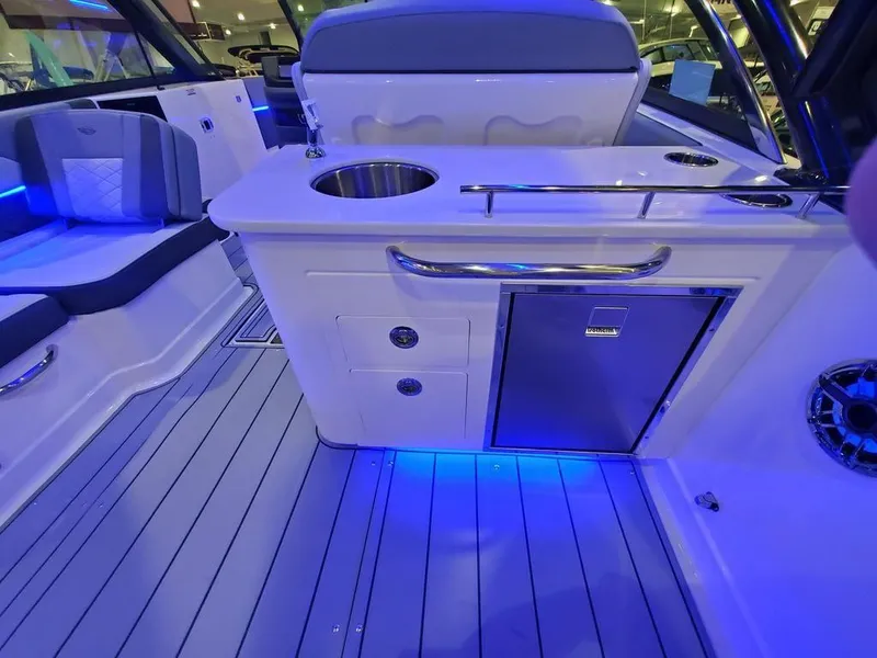 Slide: The Image of 2025 Chaparral 310 OSX boat interior with sleek seating, modern kitchenette, and ambient blue lighting. - 14