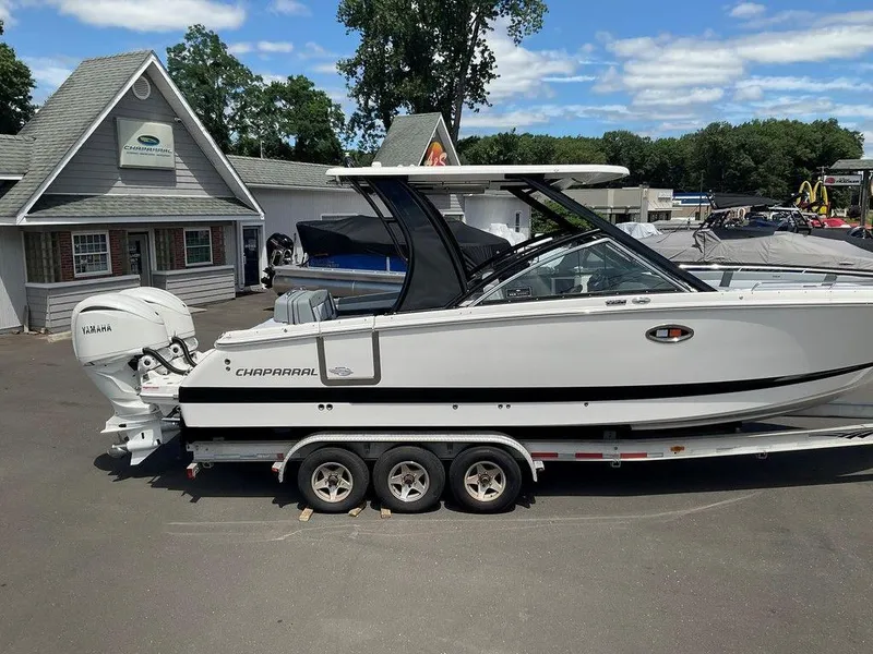 Slide: The Image of 2025 Chaparral 310 OSX boat on trailer, parked outside dealership under clear sky. - 2