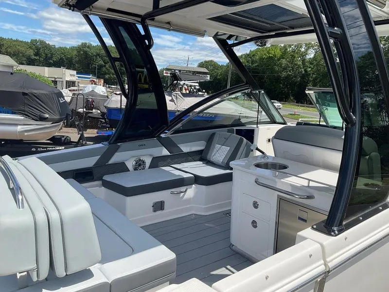 Slide: The Image of 2025 Chaparral 310 OSX boat interior with seating and kitchenette, docked outdoors. - 34