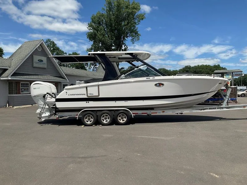 Slide: The Image of 2025 Chaparral 310 OSX boat on trailer, parked outside dealership under blue sky. - 4