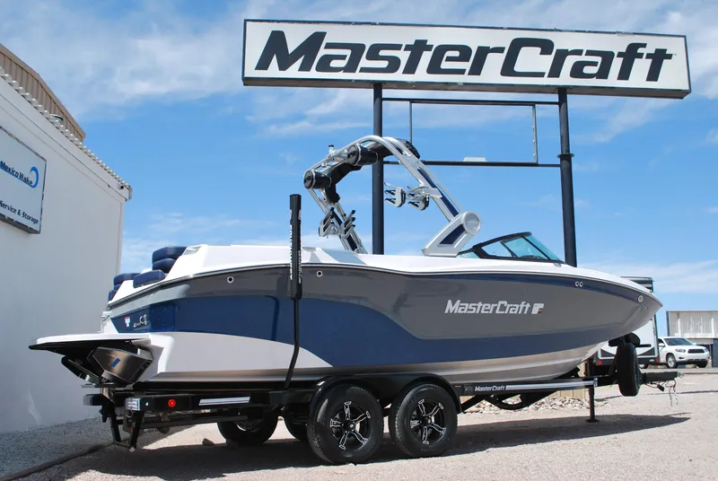 Slide: The Image of 2024 MasterCraft XT24 boat on trailer under dealership sign. - 0