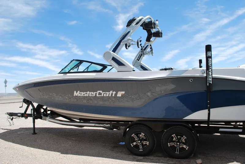 Slide: The Image of 2024 MasterCraft XT24 boat on trailer under clear blue sky. - 2