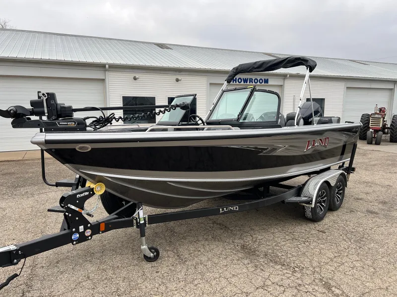 Slide: The Image of 2025 Lund 1975 Tyee boat on trailer outside showroom, black and silver design. - 2
