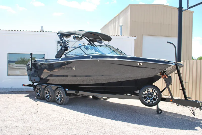Slide: The Image of 2024 MasterCraft X26 boat on trailer, sleek black design, parked outdoors. - 0